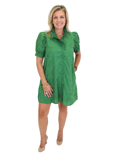 Model wearing green floral embroidered dress with hand in side pocket, front.
