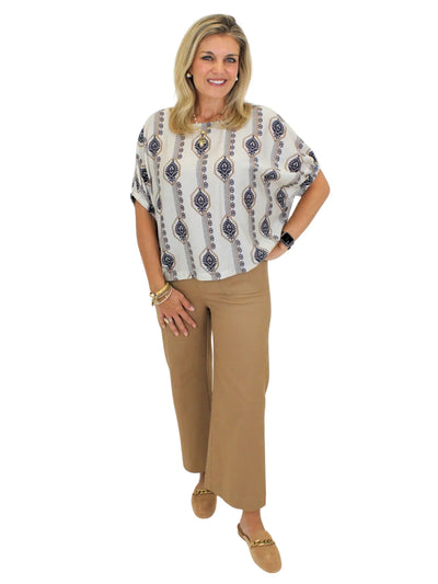 Model wearing geometric floral blouse with tan pants and shoes on white background, front.