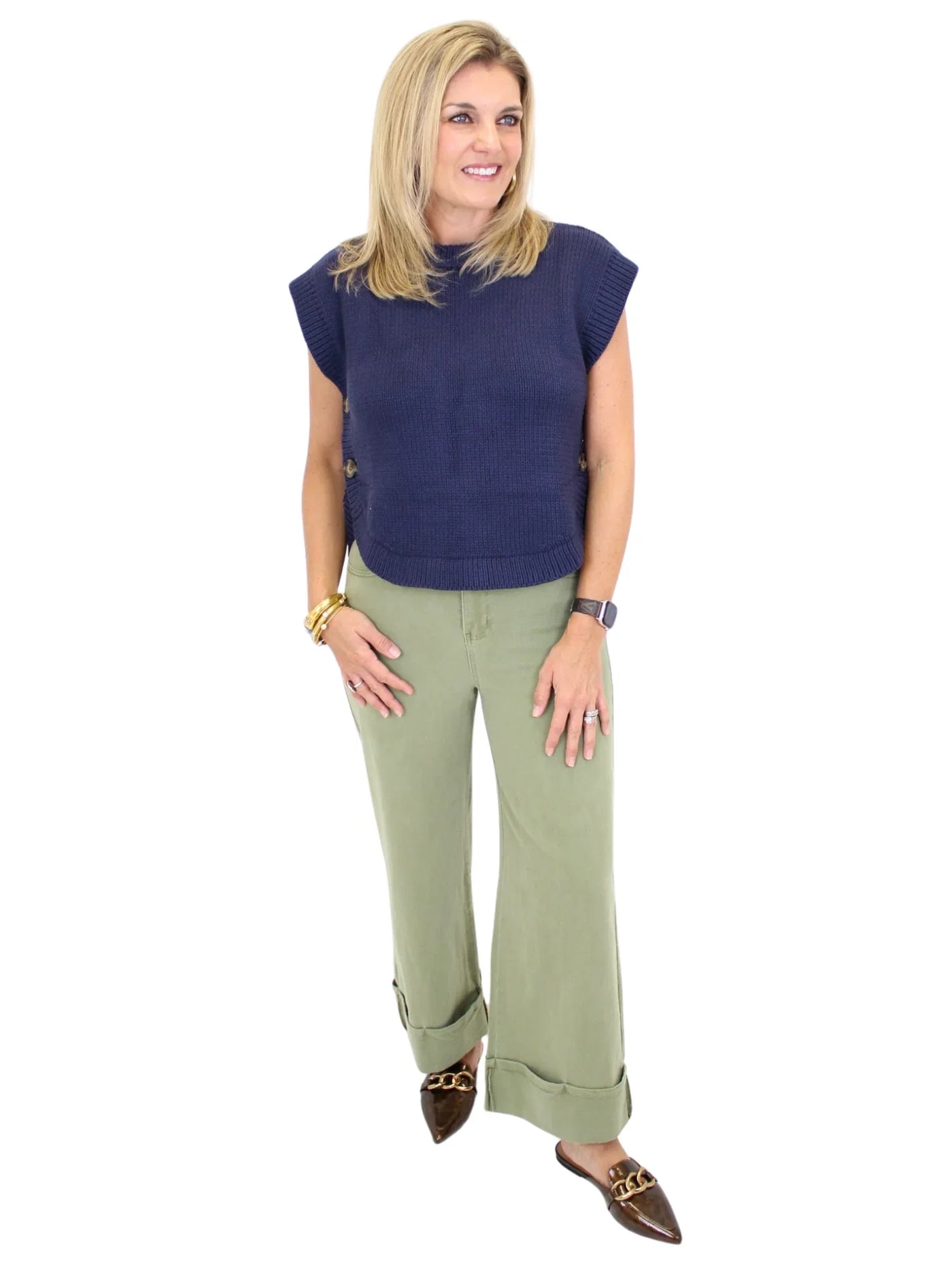 Woman wearing a navy blue sleeveless sweater and green pants on a white background, font.