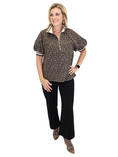 Woman wearing a leopard print shirt with striped collar and cuffs on a white background, angled front.