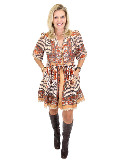 Woman wearing an ornate patterned dress with brown boots on a white background, front.