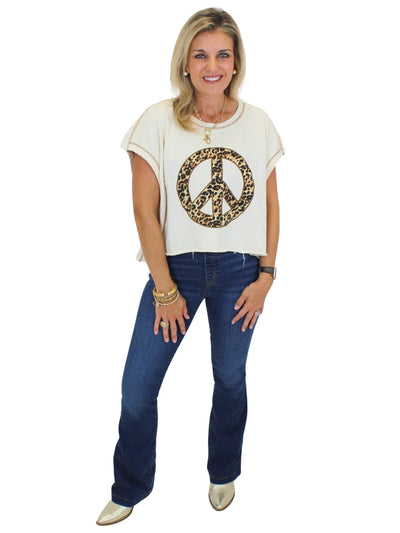 Model wearing cheetah print peace sign top with jeans on white background, front.
