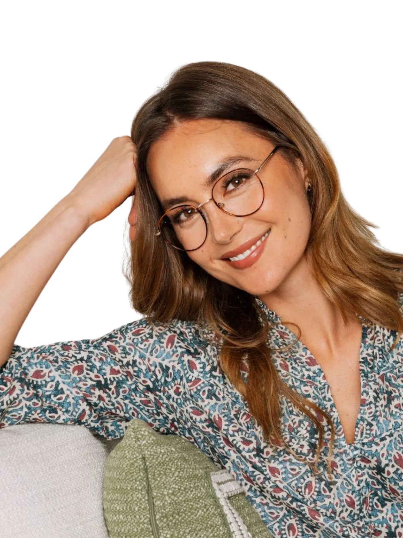 Woman wearing round tortoiseshell glasses and a patterned shirt on a white background.