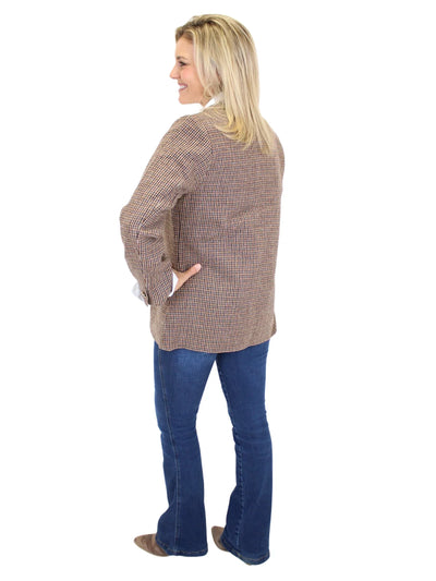 Woman wearing a brown plaid blazer and blue jeans on a white background, back.