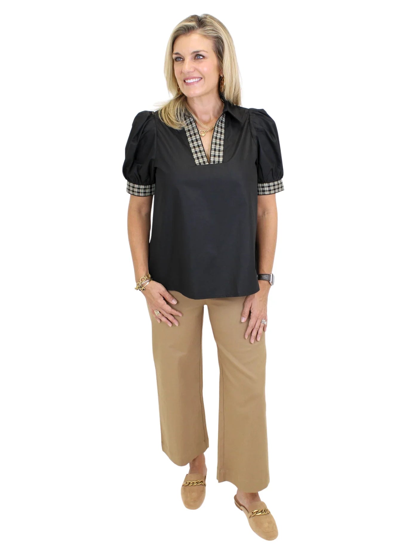 Model wearing black top with plaid trim and tan pants on white background, angled front.