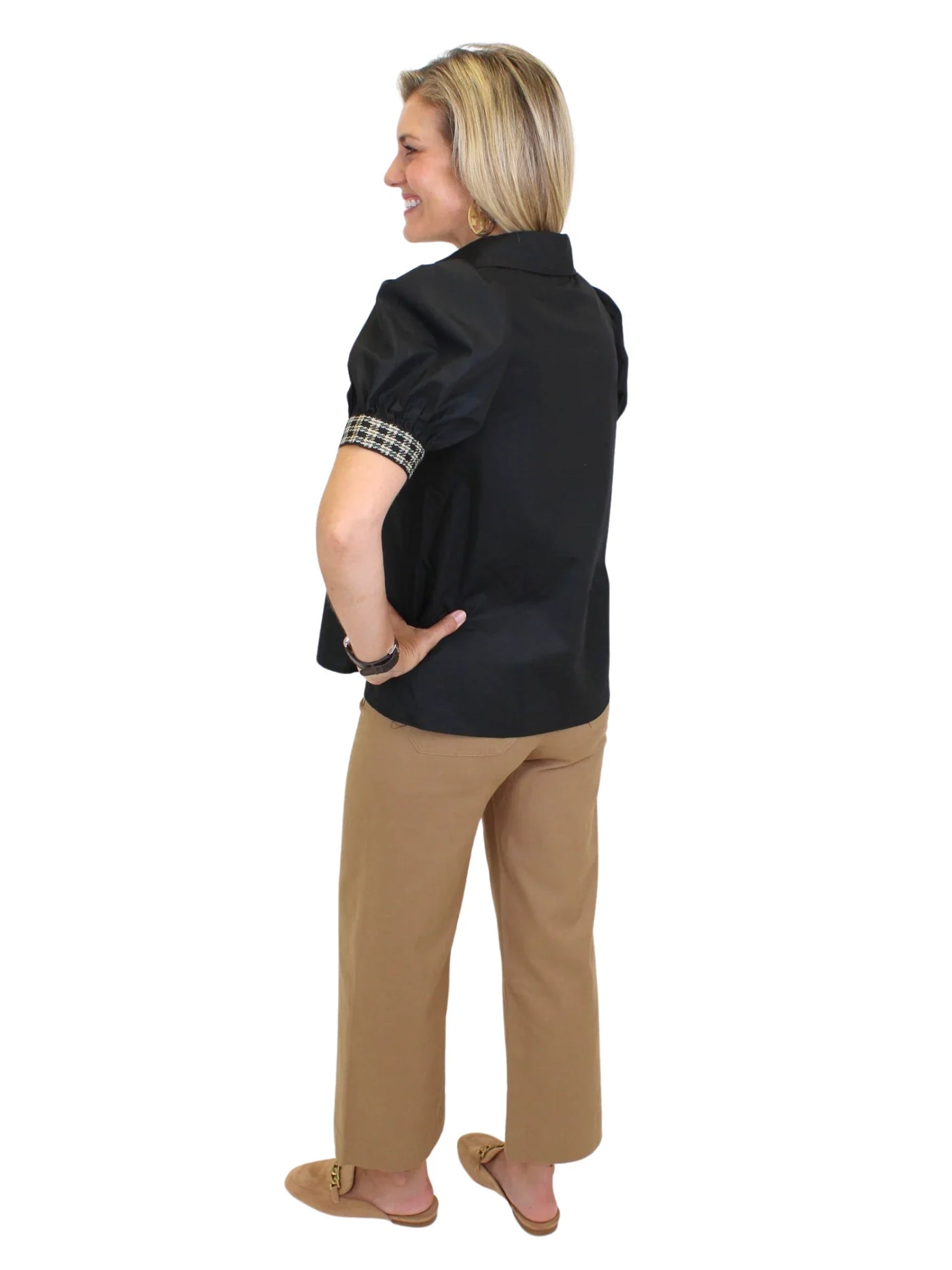 Model wearing black top with plaid trim and tan pants on white background, back.