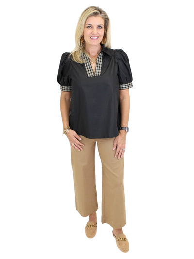 Model wearing black top with plaid trim and tan pants on white background, front.