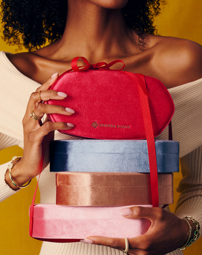 Person holding a stack of colorful gift boxes with a visible brand logo.