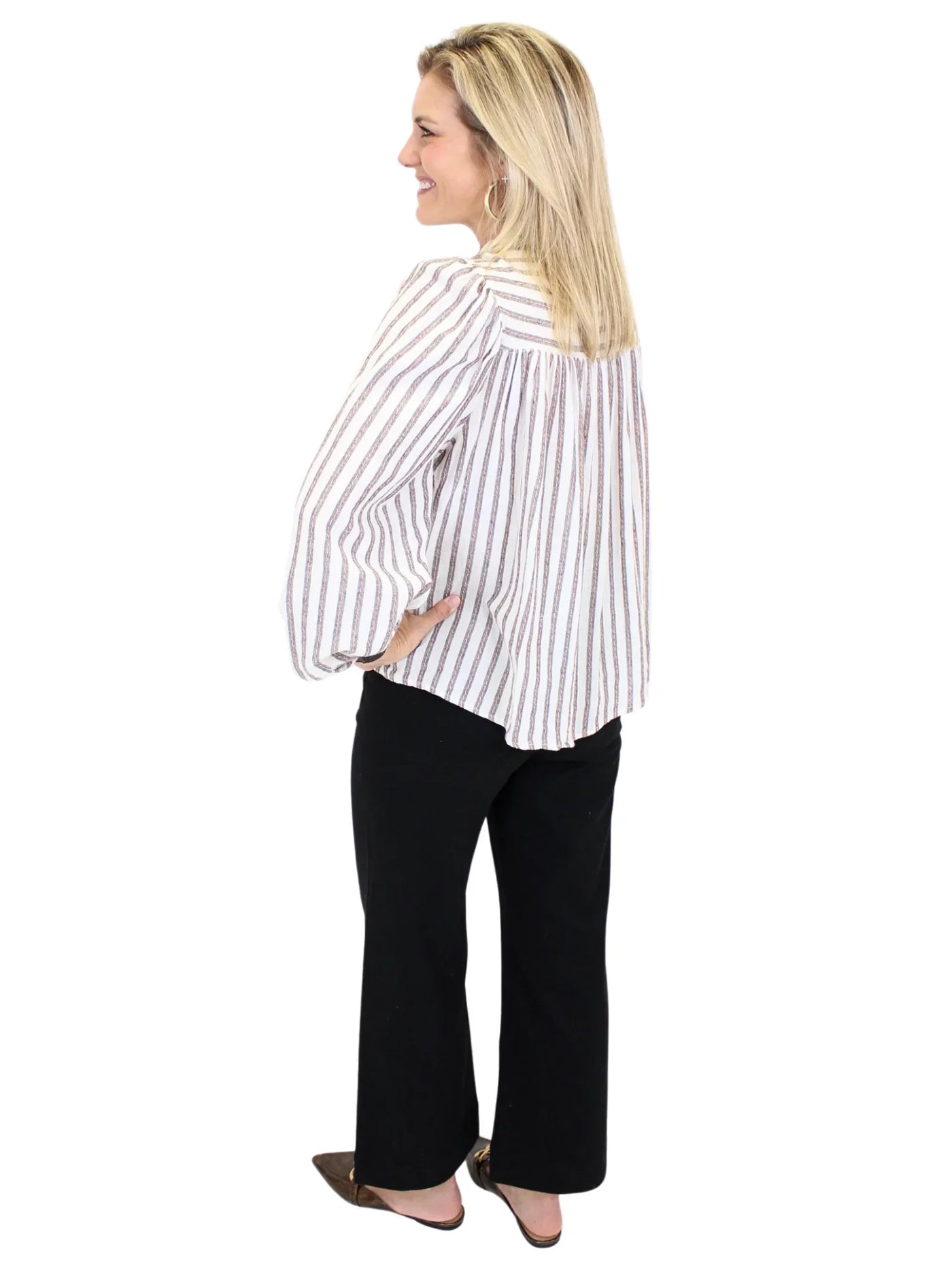 Woman wearing a striped shirt and black pants on a white background, back.