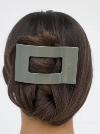 Woman with a bun holding a green hair clip against a white background.