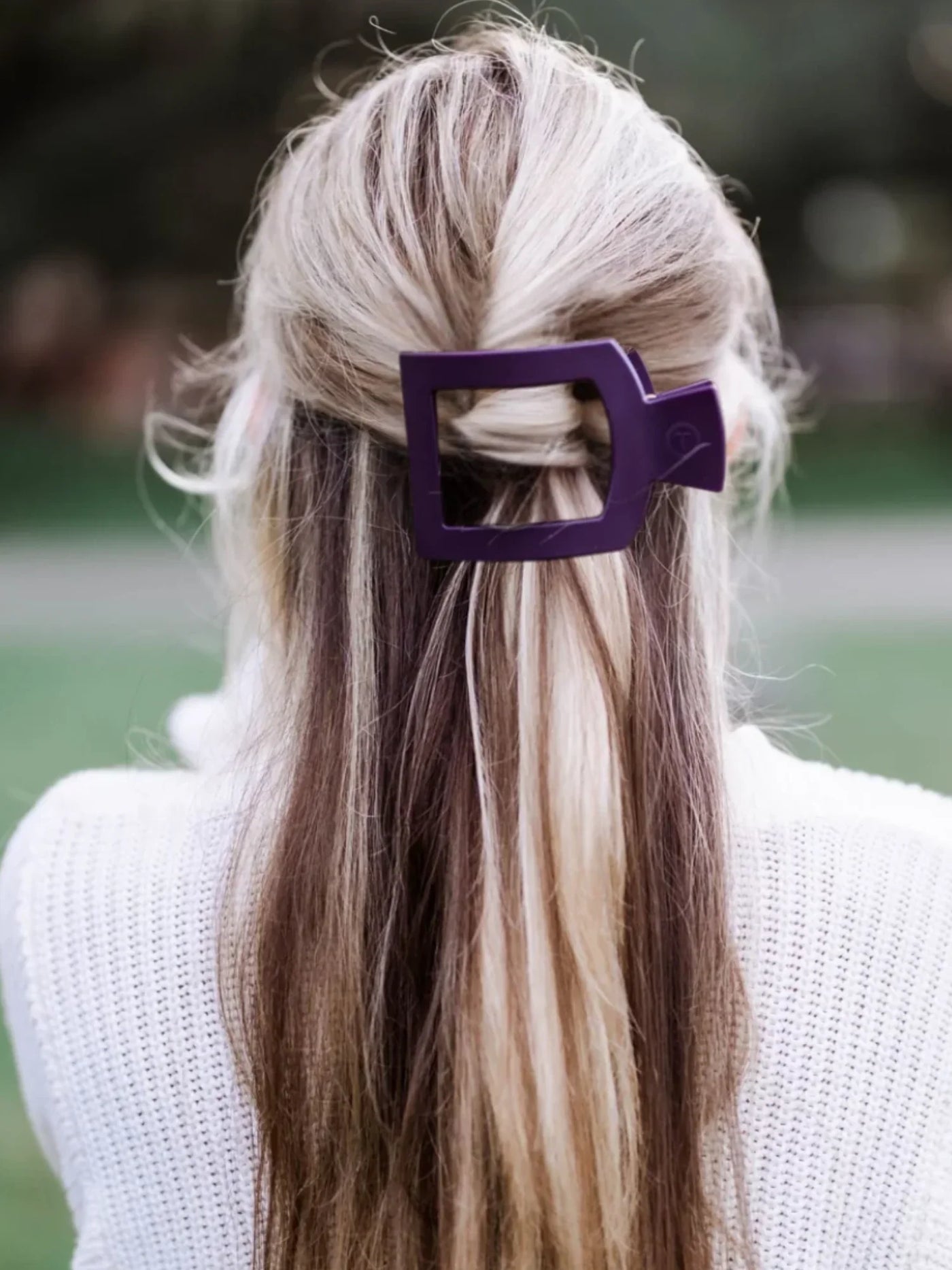 Person with long, styled hair featuring a large burgundy hair clip against a blurred outdoor background.