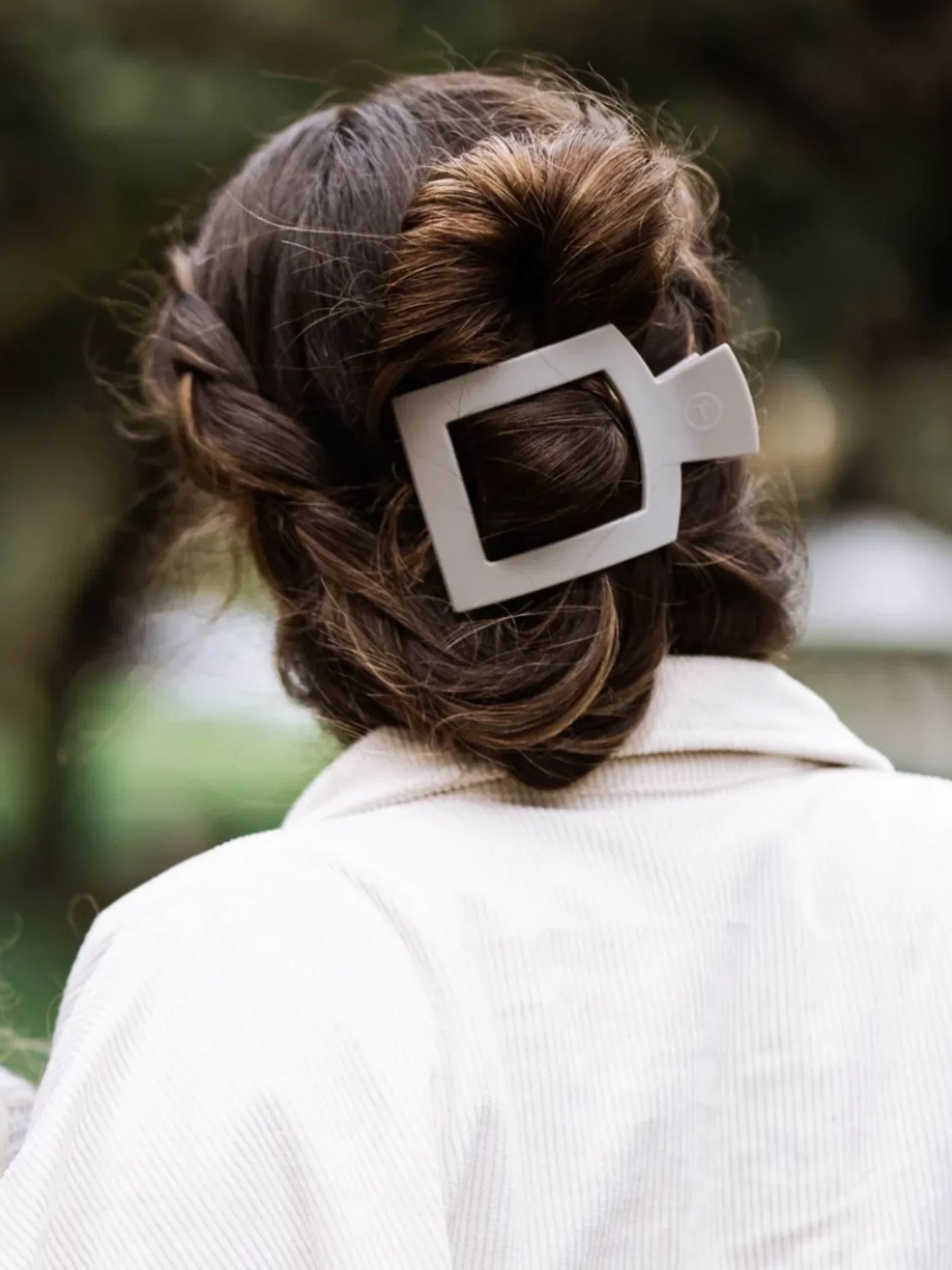 Light grey large square hair clip in woman's twisted updo.