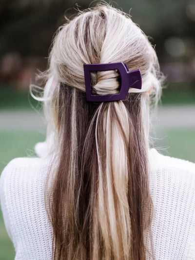 Person with long, wavy hair tied back with a purple hair clip, wearing a white sweater.