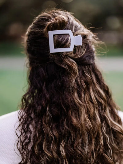 Light grey medium square hair clip in woman's wavy half-up hair.