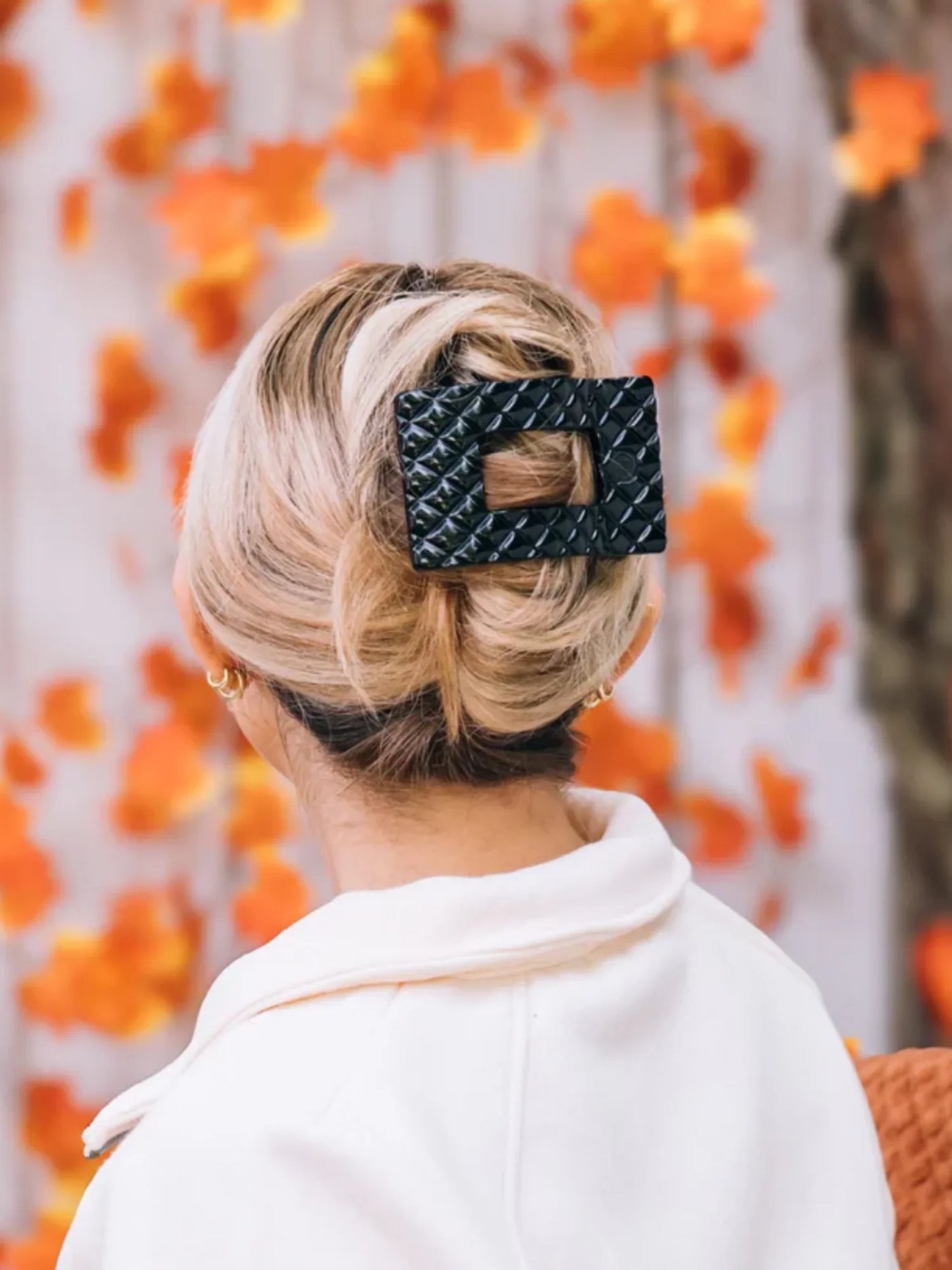 Woman with hair in updo featuring a black rectangular hair accessory against an orange leafy background.