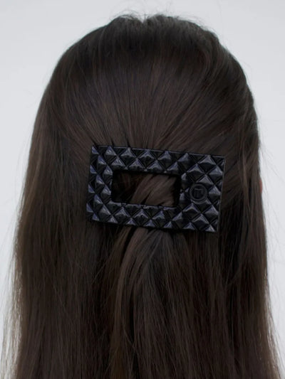 Black quilted small rectangle hair clip in woman's hair on white background.
