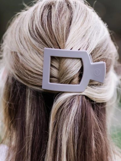Light grey small square hair clip in woman's half-up hair.