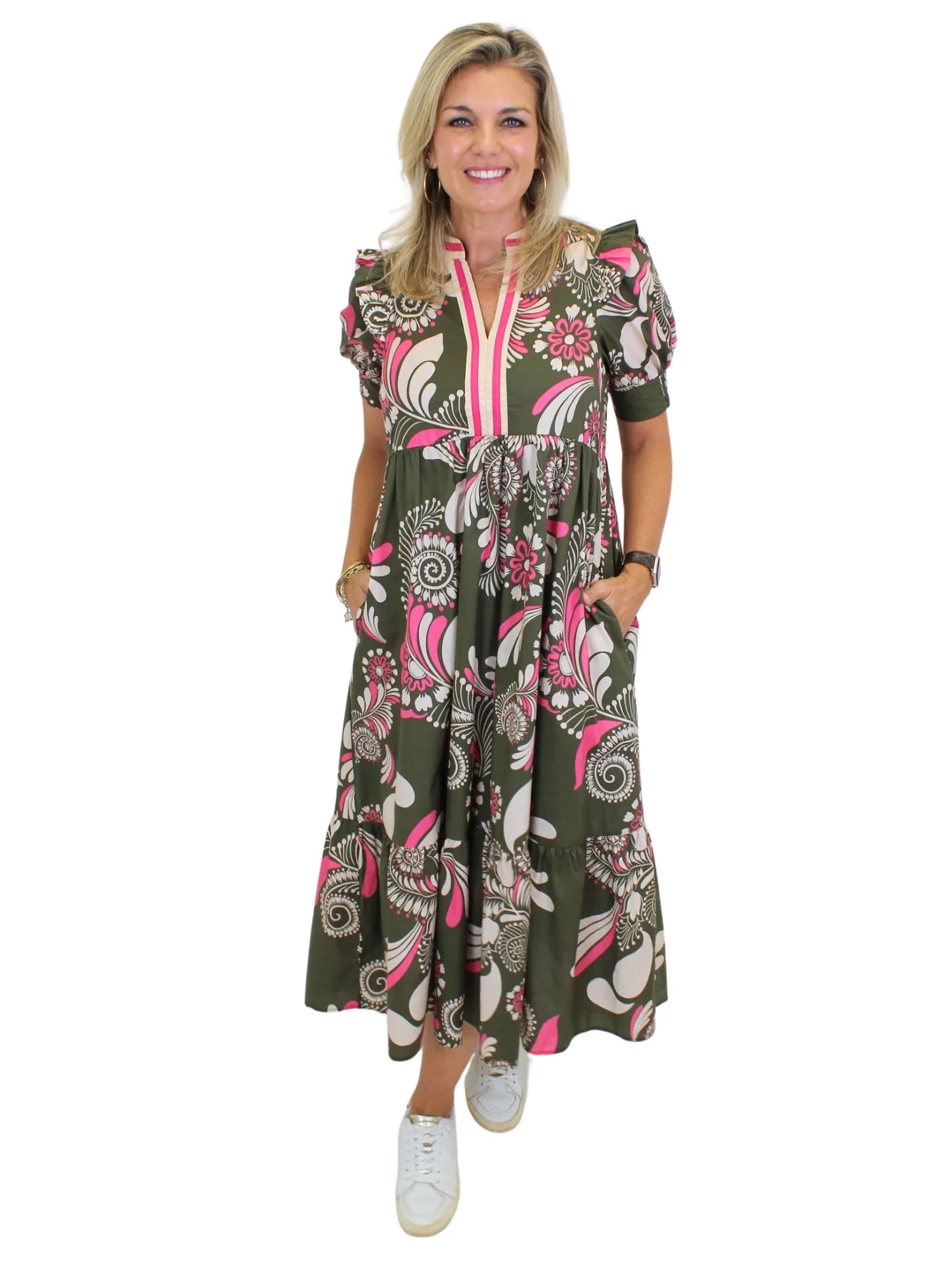 Model wearing green and pink floral midi dress with hands in pockets on white background, front.