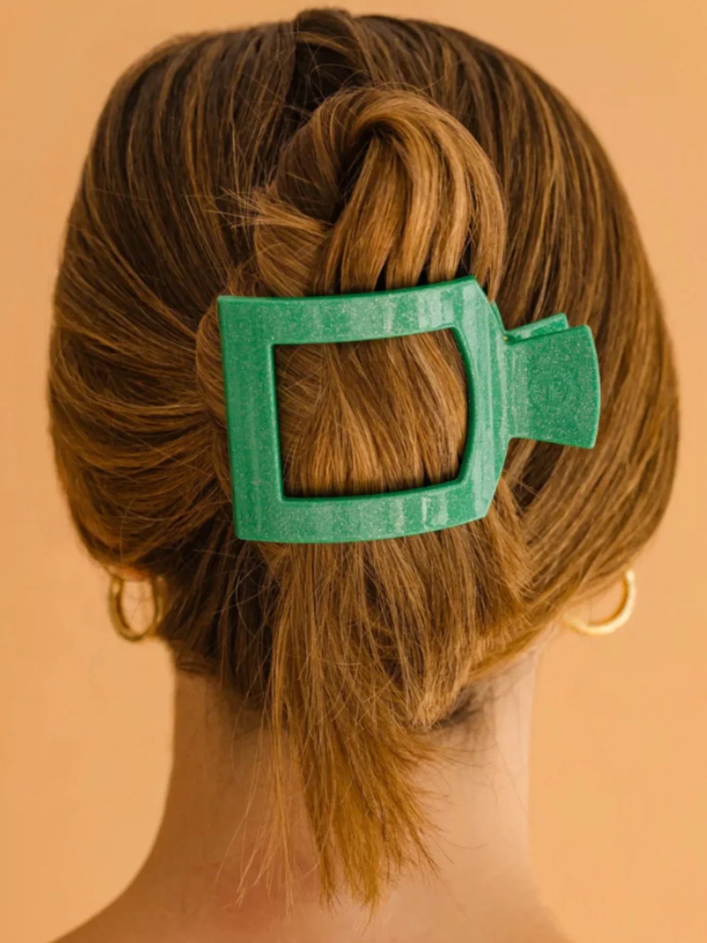 Sparkly green square hair clip in a person's hair against a beige background.