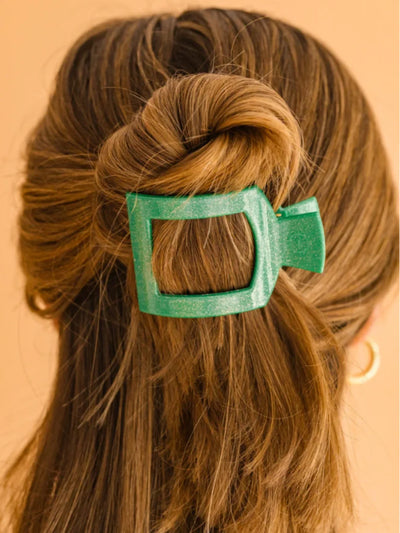 Sparkly green square hair clip in a person's hair against a beige background.