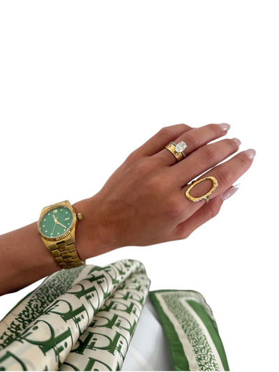 Hand wearing gold open oval ring on white background, front view.