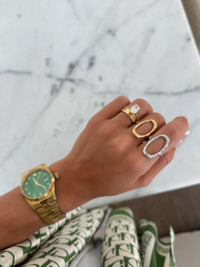 Hand wearing gold and silver open oval rings on marble background, front view.
