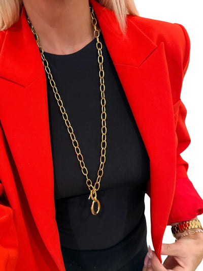 Model in red blazer wearing long gold chain necklace with toggle and oval pendant.