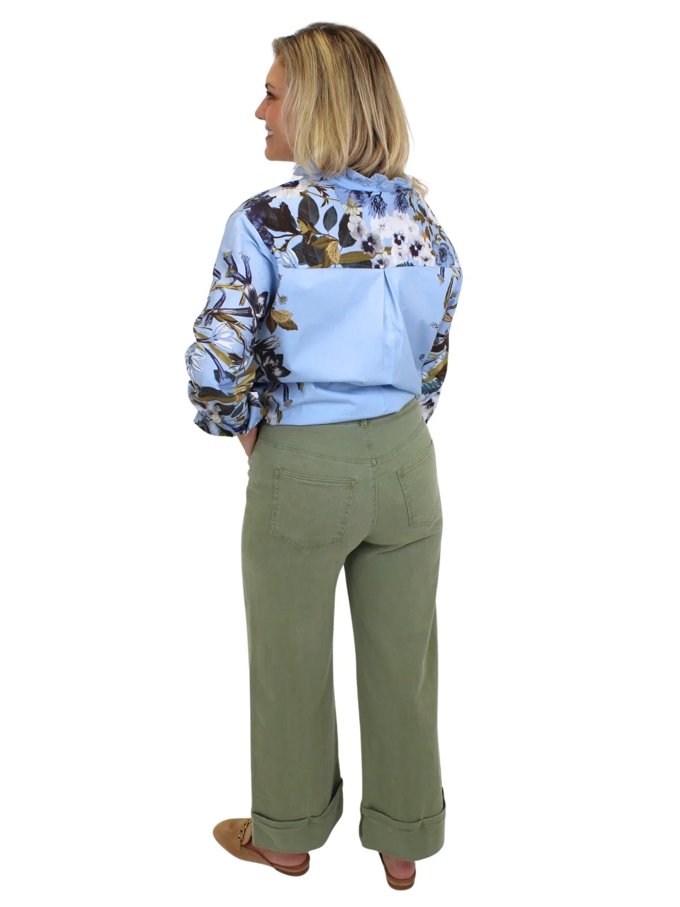 Model wearing blue blouse tucked into green wide leg cuffed jeans on white background, back.