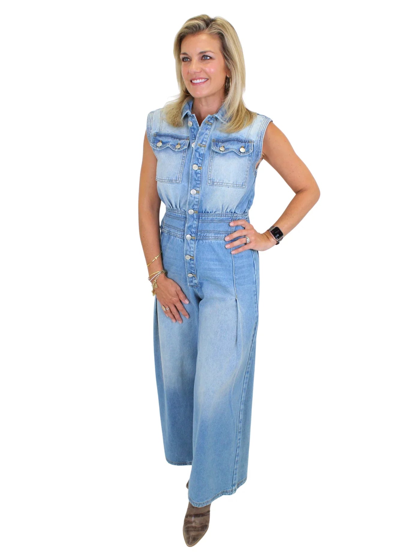 Model wearing wide leg denim jumpsuit with hand on hip on white background, front angled.