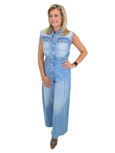 Model wearing wide leg denim jumpsuit with hand on hip on white background, front angled.