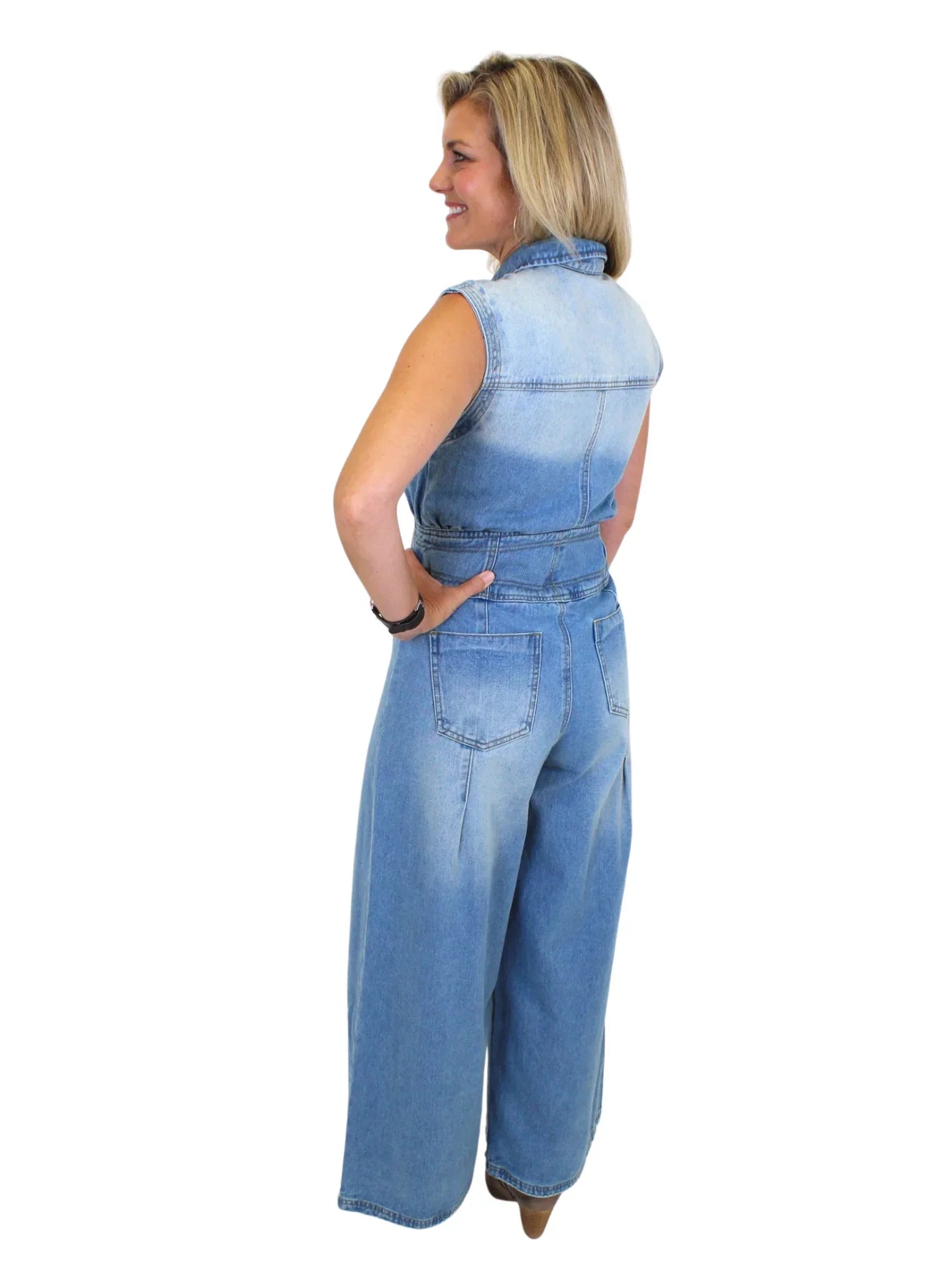 Model wearing wide leg denim jumpsuit with hand on hip on white background, back.