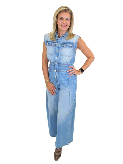 Model wearing wide leg denim jumpsuit with hand on hip on white background, front.