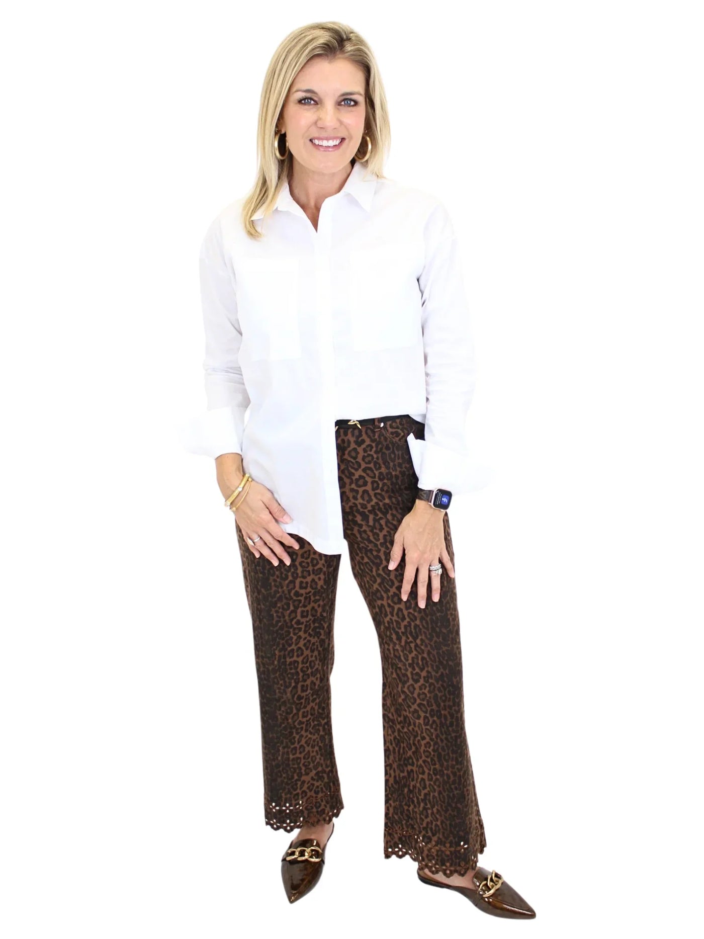 Woman wearing leopard print pants and white blouse on a white background, front.