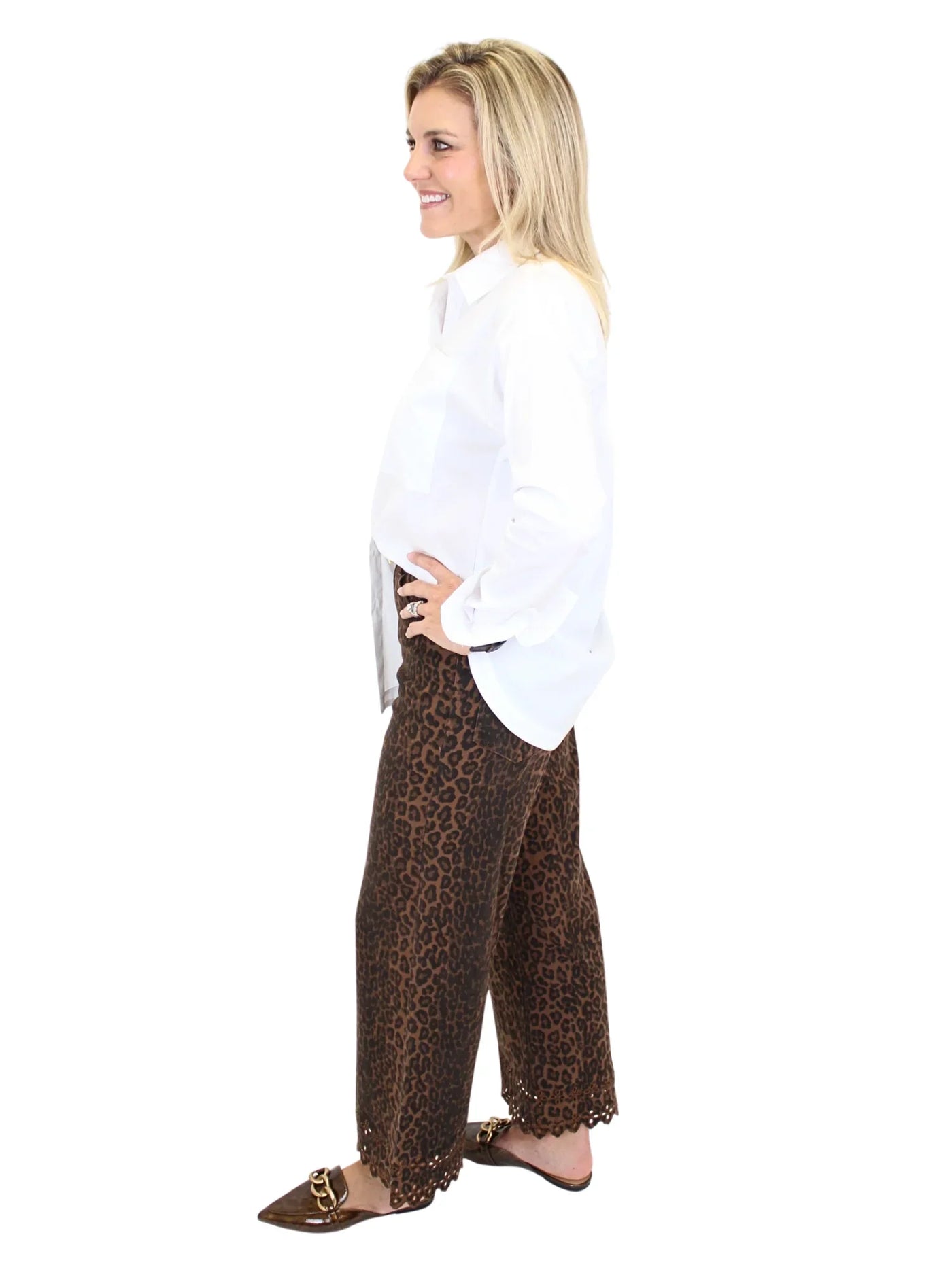 Woman wearing leopard print pants and white blouse on a white background, side.