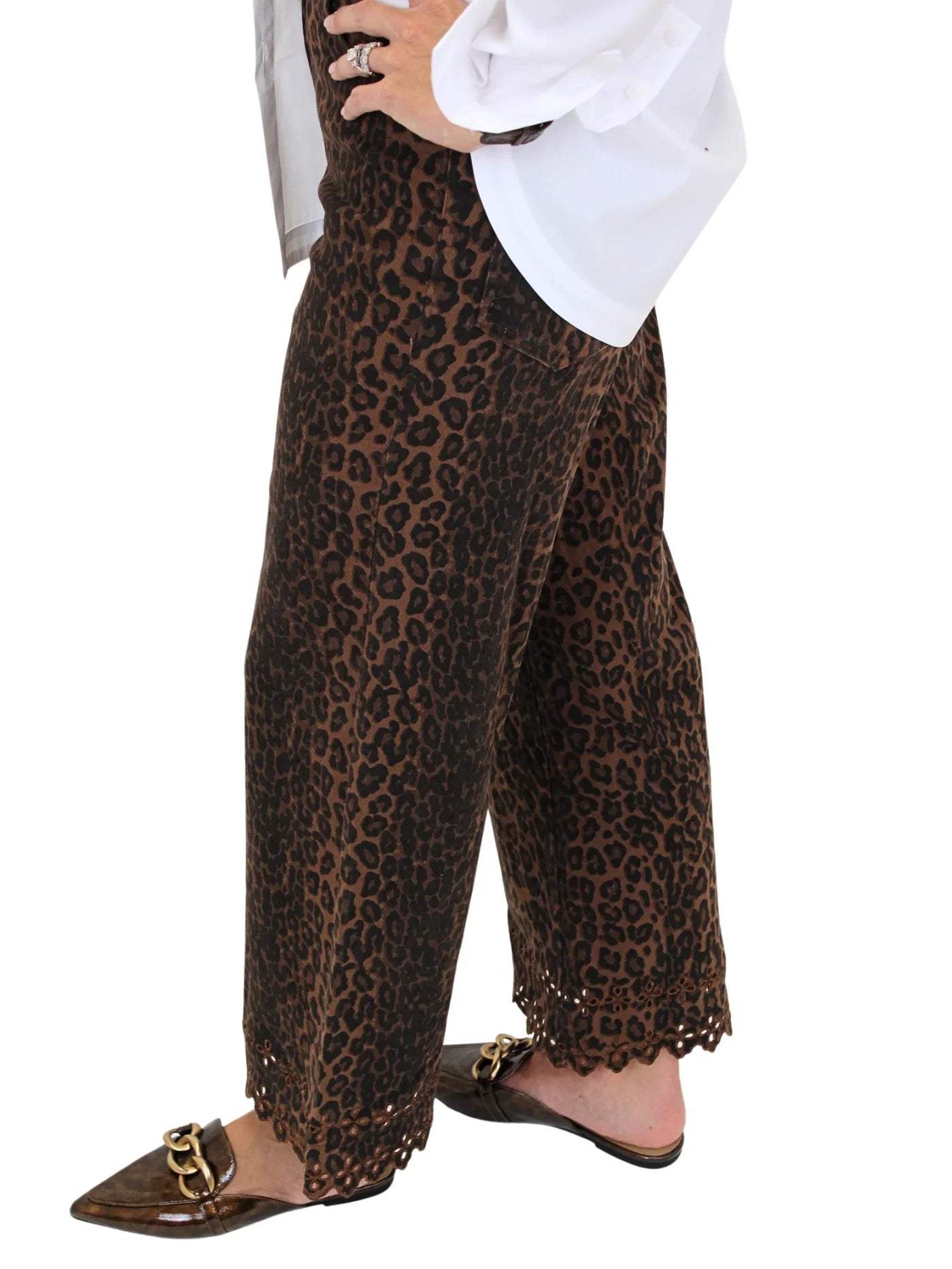 Woman wearing leopard print pants with eyelet hem details on a white background, closeup side.
