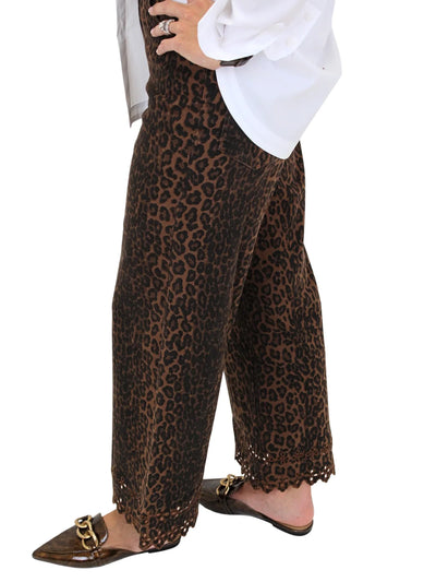 Woman wearing leopard print pants with eyelet hem details on a white background, closeup side.