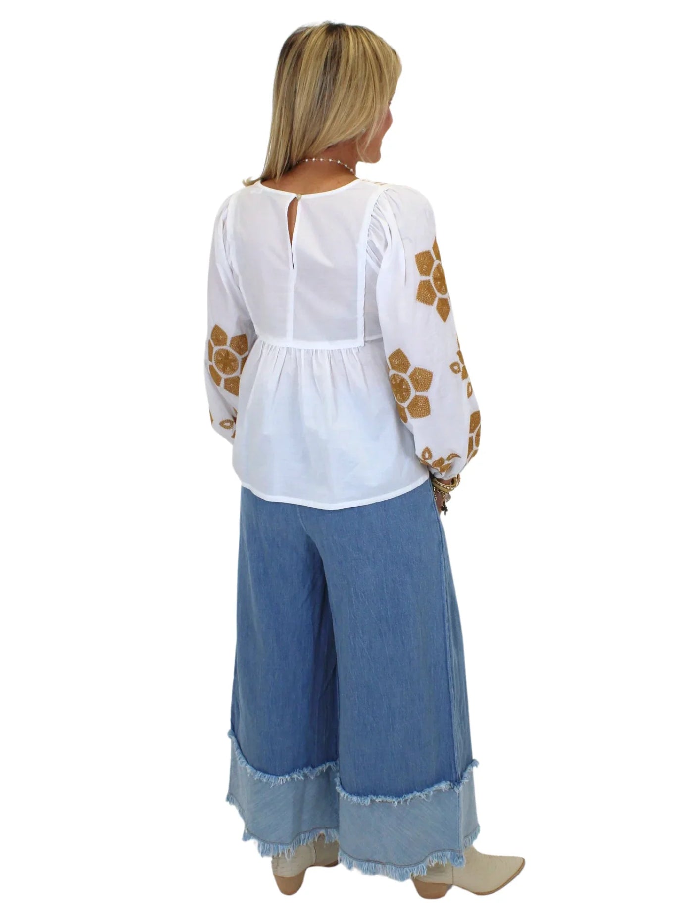 Model wearing tan embroidered white babydoll blouse and wide leg blue jeans on white background, back.