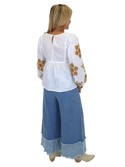 Model wearing tan embroidered white babydoll blouse and wide leg blue jeans on white background, back.