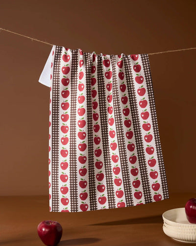Tea towel with red apple pattern hanging on a line against a brown background