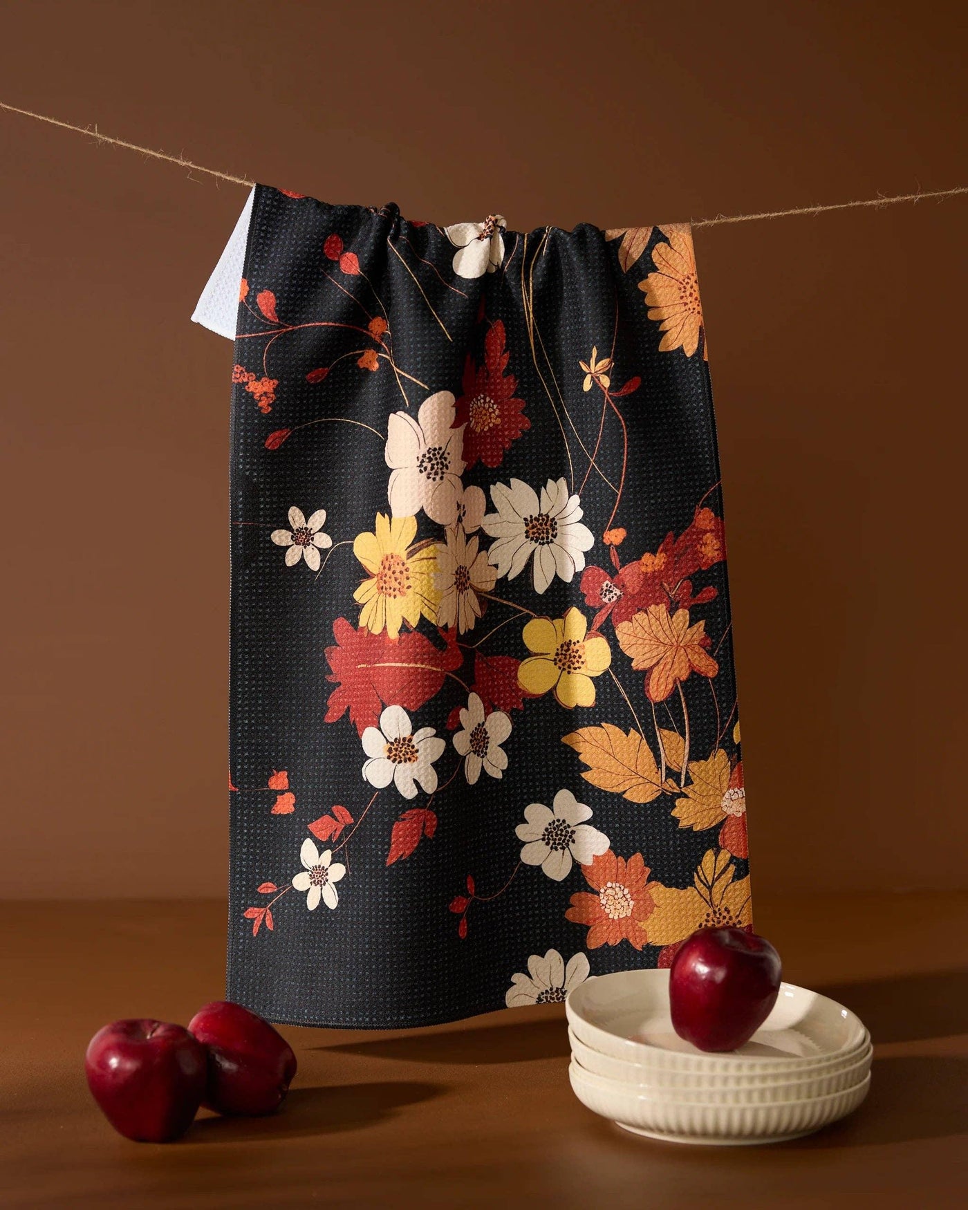 Black, red, and orange floral print tea towel hanging against a brown background.