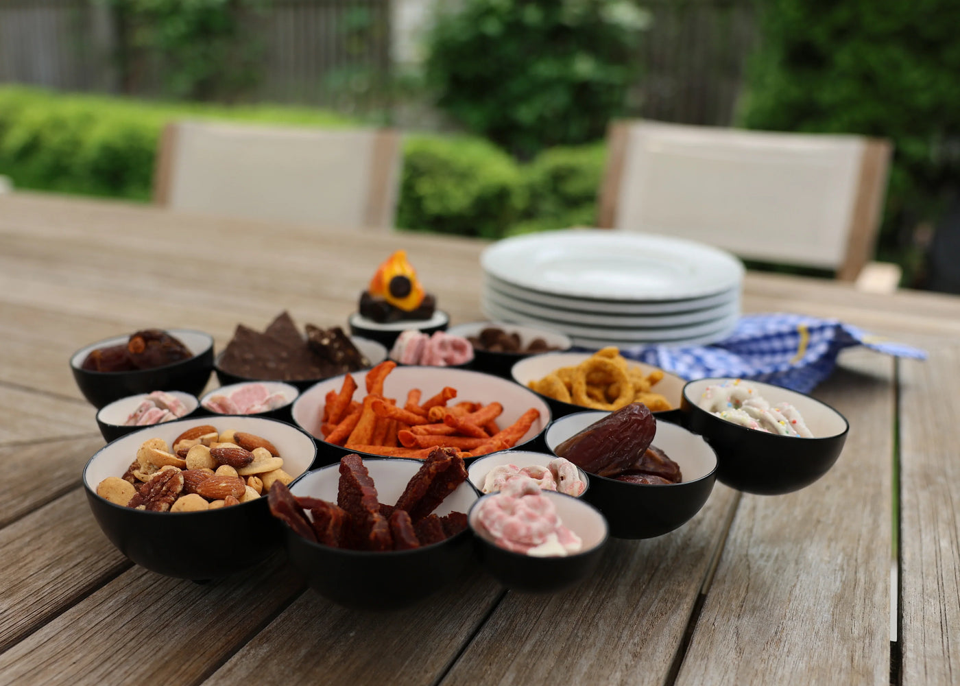 Assorted snacks in small bowls on a wooden table outdoors.
