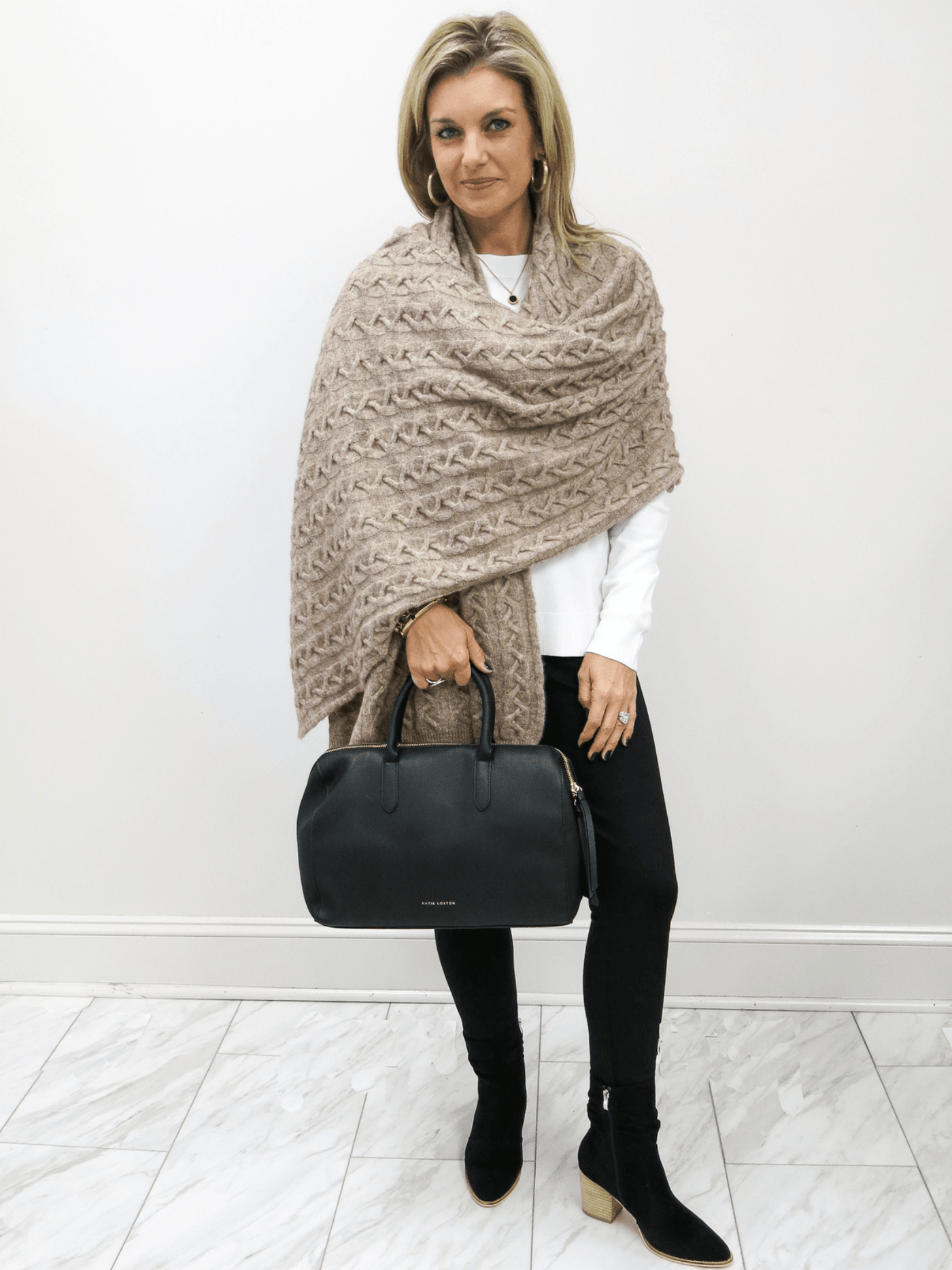 Full view of Kerisma taupe sweater wrap with white Charlie Paige top, black Charlie Paige pants, black Charie Paige boots and black Katie Loxton handbag. .