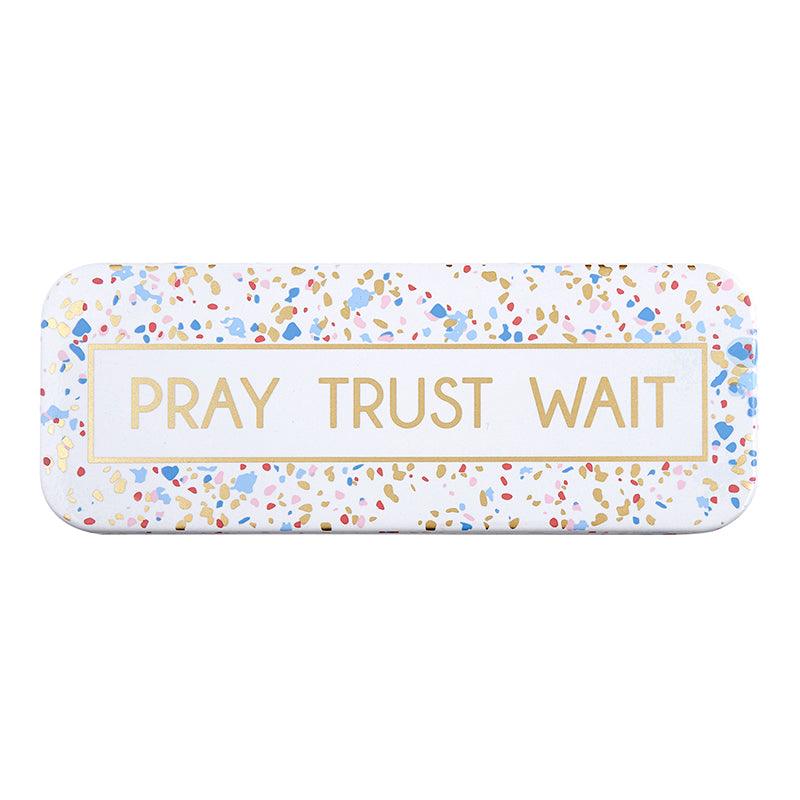 Enamel plaque with a white background, blue, pink, gold, and red confetti with "pray trust wait" printed on the front