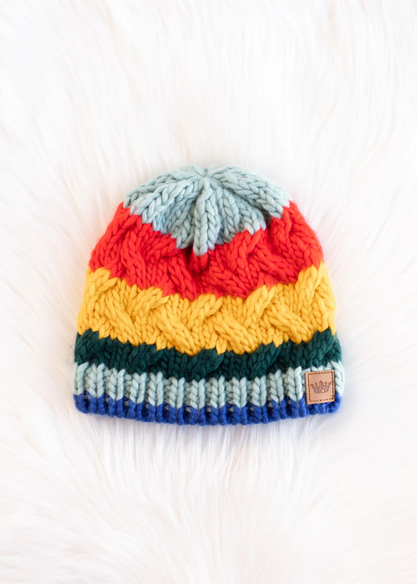 Multicolor striped cable knit beanie on white faux fur background front view.