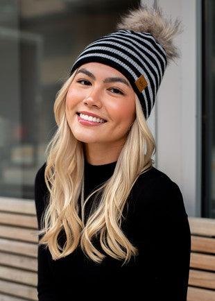 Black and gray striped beanie with faux fur pom on model front view.