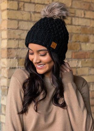 Textured fleece lined beanie with cuff and faux fur pom in black on model front view.