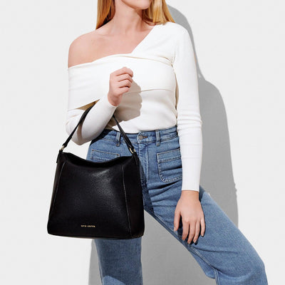 Black hand bag with fold over top on the arm of a model