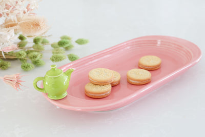 Nora Fleming Coral pink bread tray with pinstripe design and lemongrass green Nora Fleming  teapot mini with vanilla oreo cookies on tray.