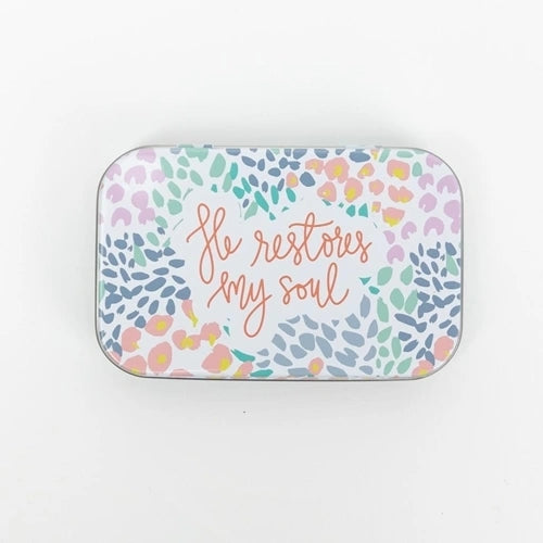 Little metal tin with "He restores my soul" labeled on the top with multicolored spots