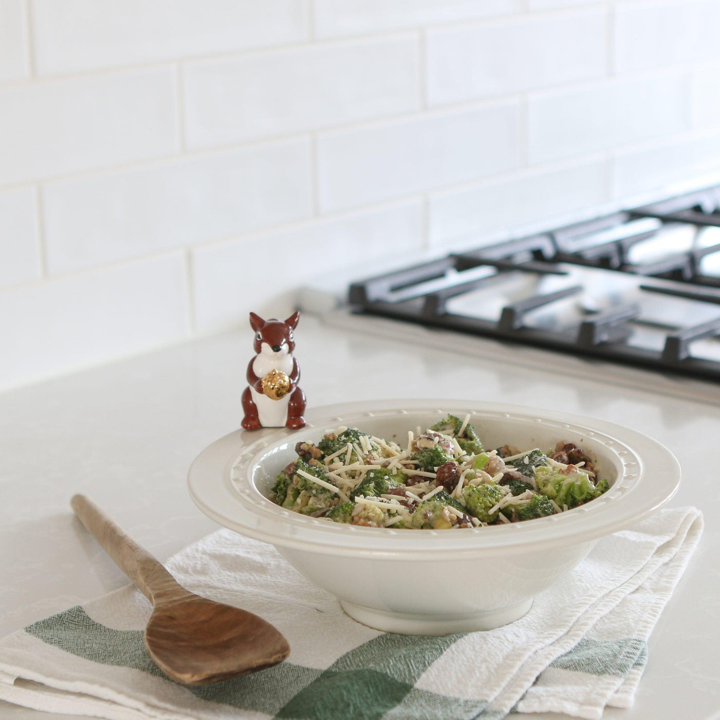 White stoneware bowl with pin dot design with broccoli salad inside and a squirrel mini